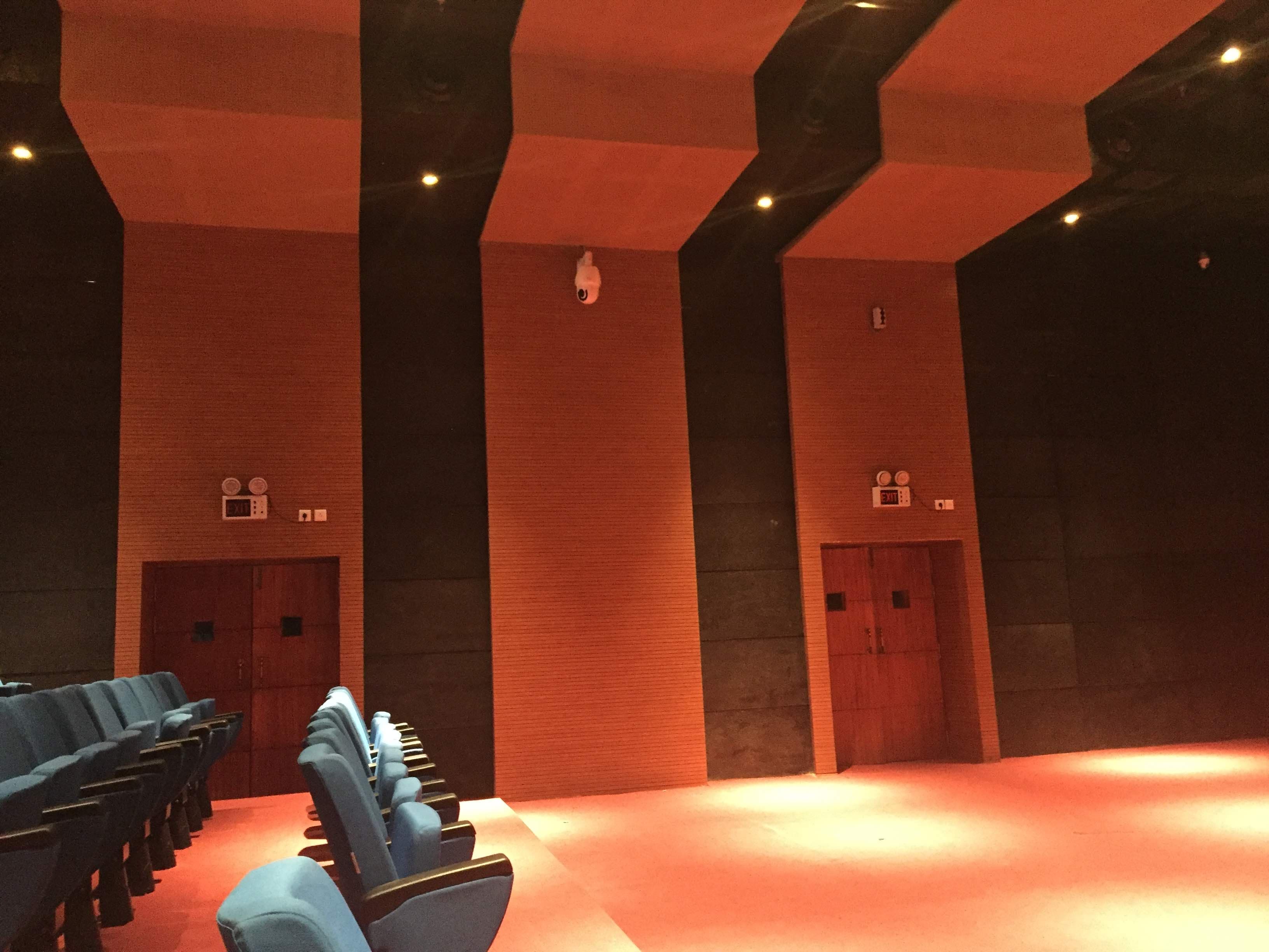 Multi-Purpose Hall Itanagar — completed house side wall with Prolite emergency-exit doors, EXIT signage and blue tiered seating