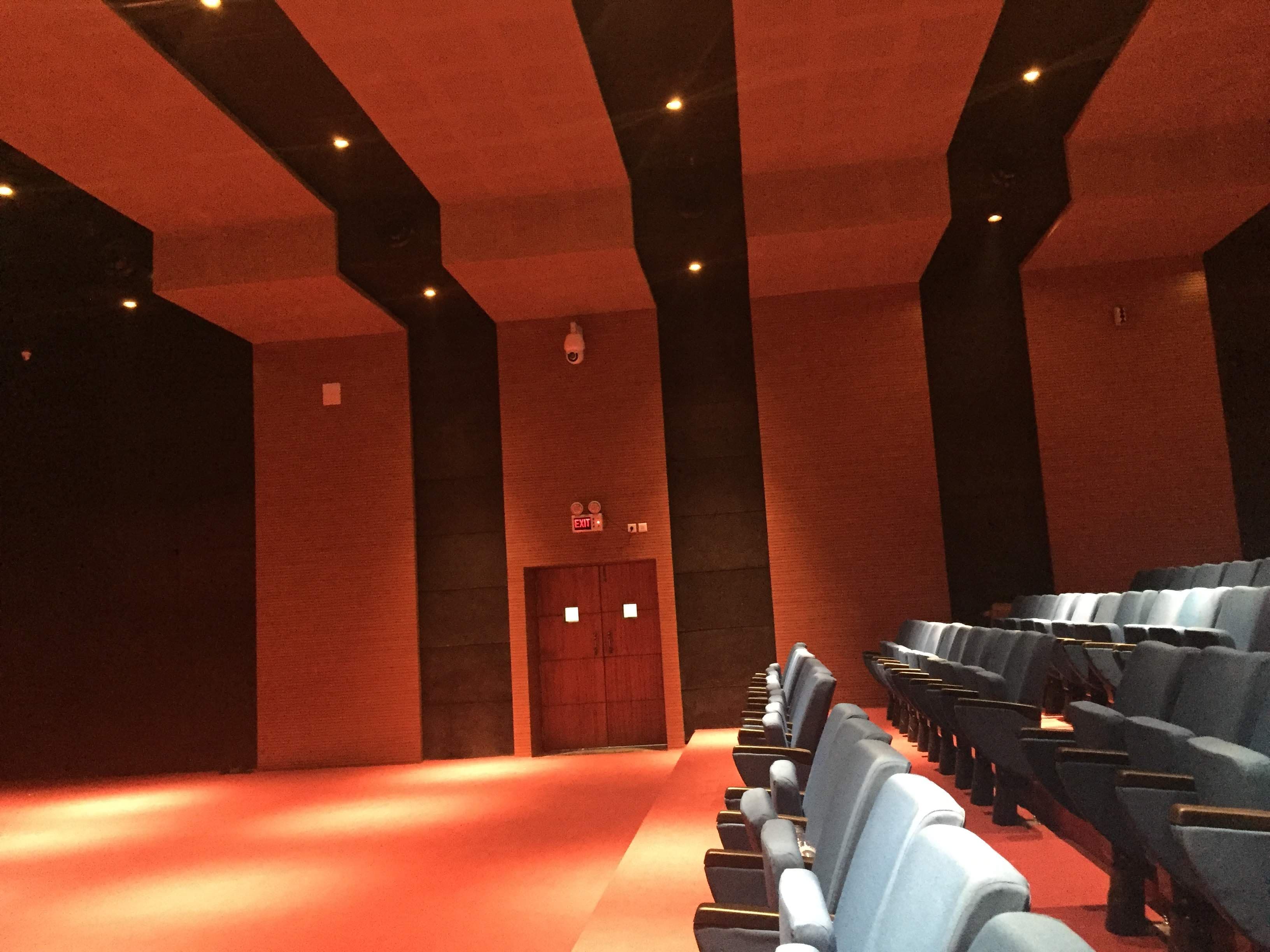 Multi-Purpose Hall Itanagar — rear emergency-exit door with Prolite EXIT signage, stepped ceiling and blue tiered seating
