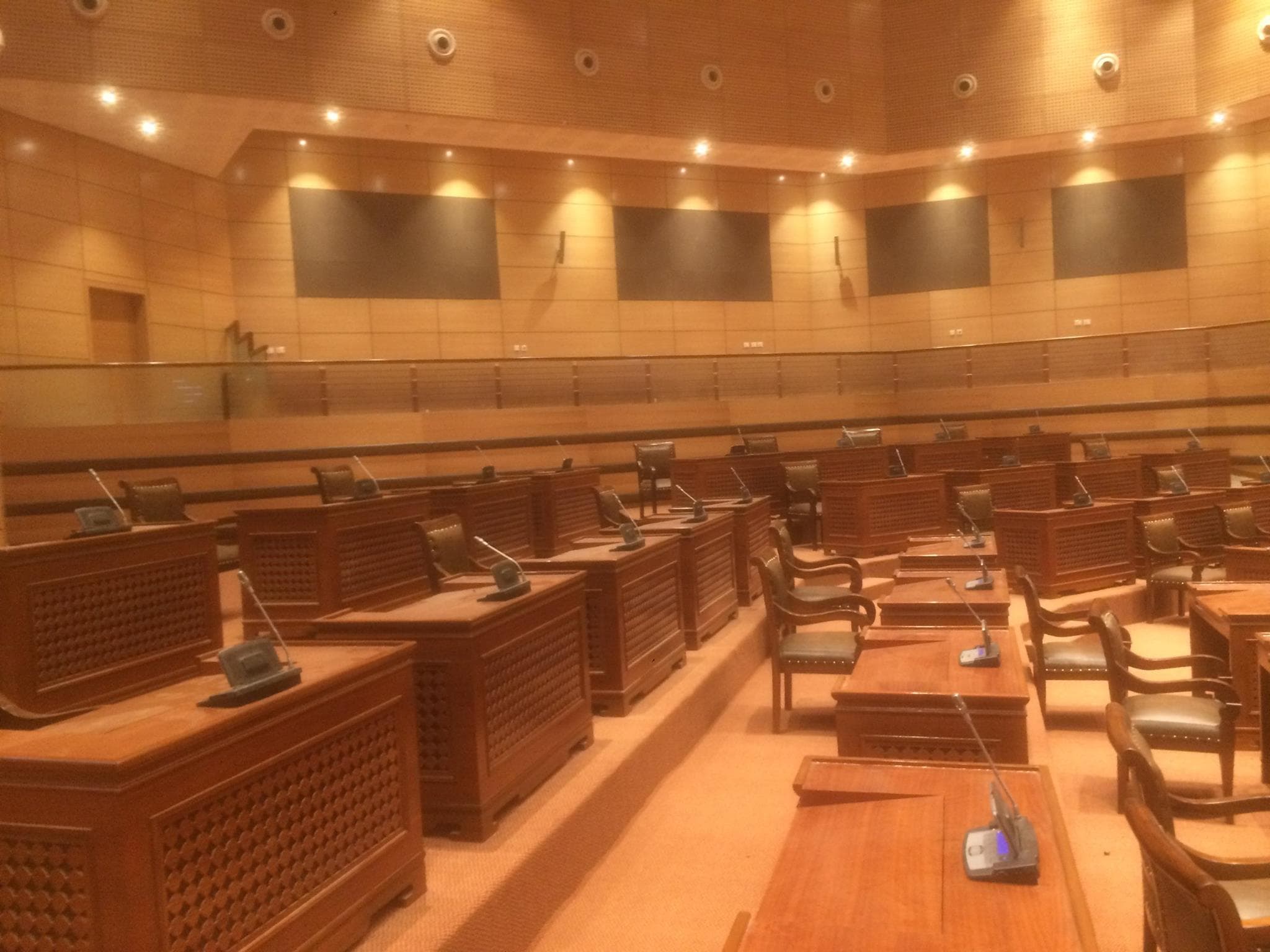 Concentric rows of teak delegate desks with Bosch DCN microphones, focused chamber lighting during a vote.